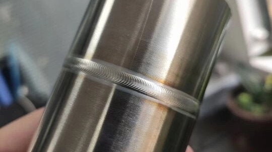 Silver white weld seam with smooth surface and uniform finish created by precision automatic welding machine on stainless steel component.
